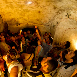 En grupp människor i ett svagt upplyst, välvt underjordiskt rum som tittar upp i taket, med en person som håller i en ficklampa.