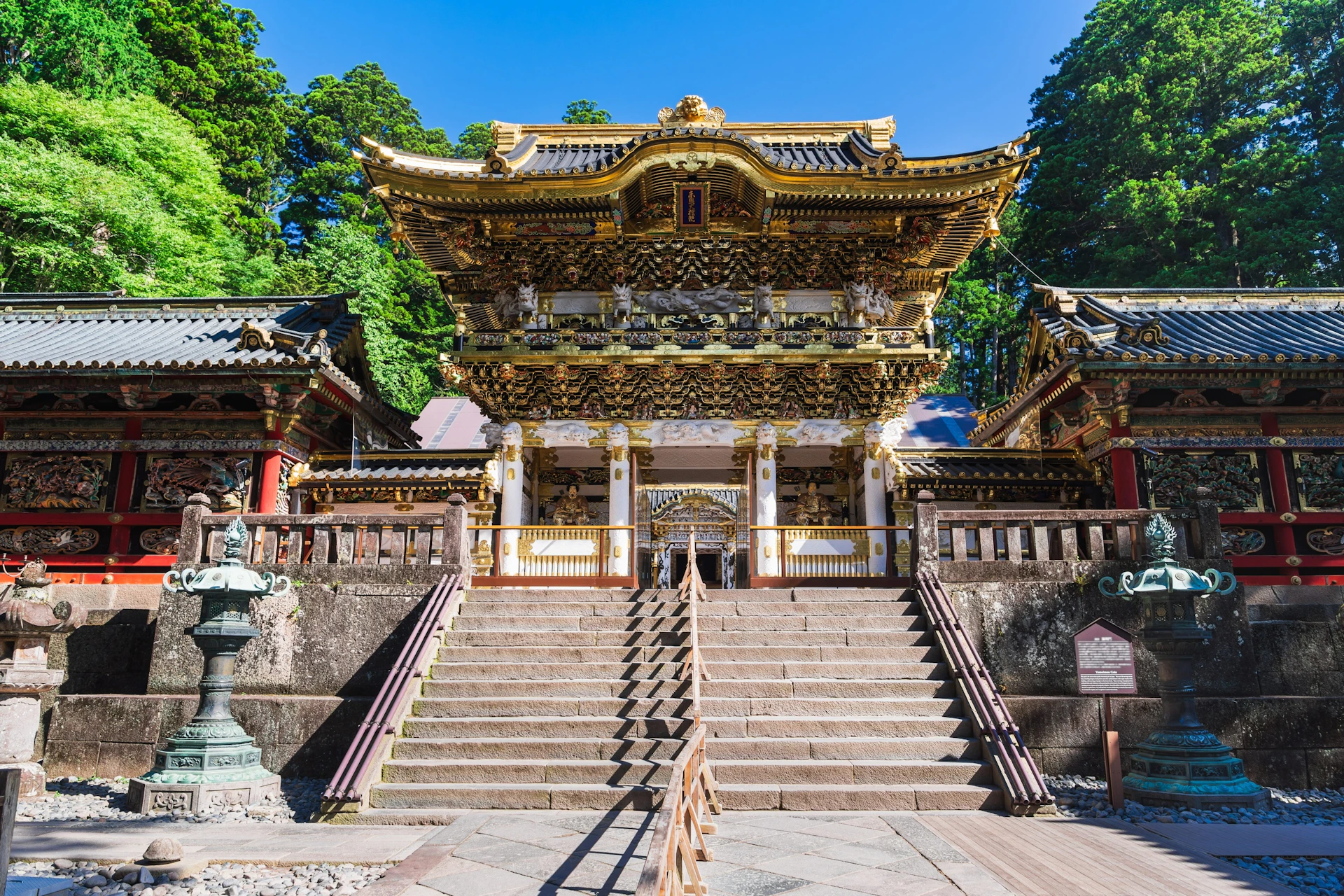 Ornate traditional Japanese temple with golden details, viewed from stone stairs under a clear blue sky.