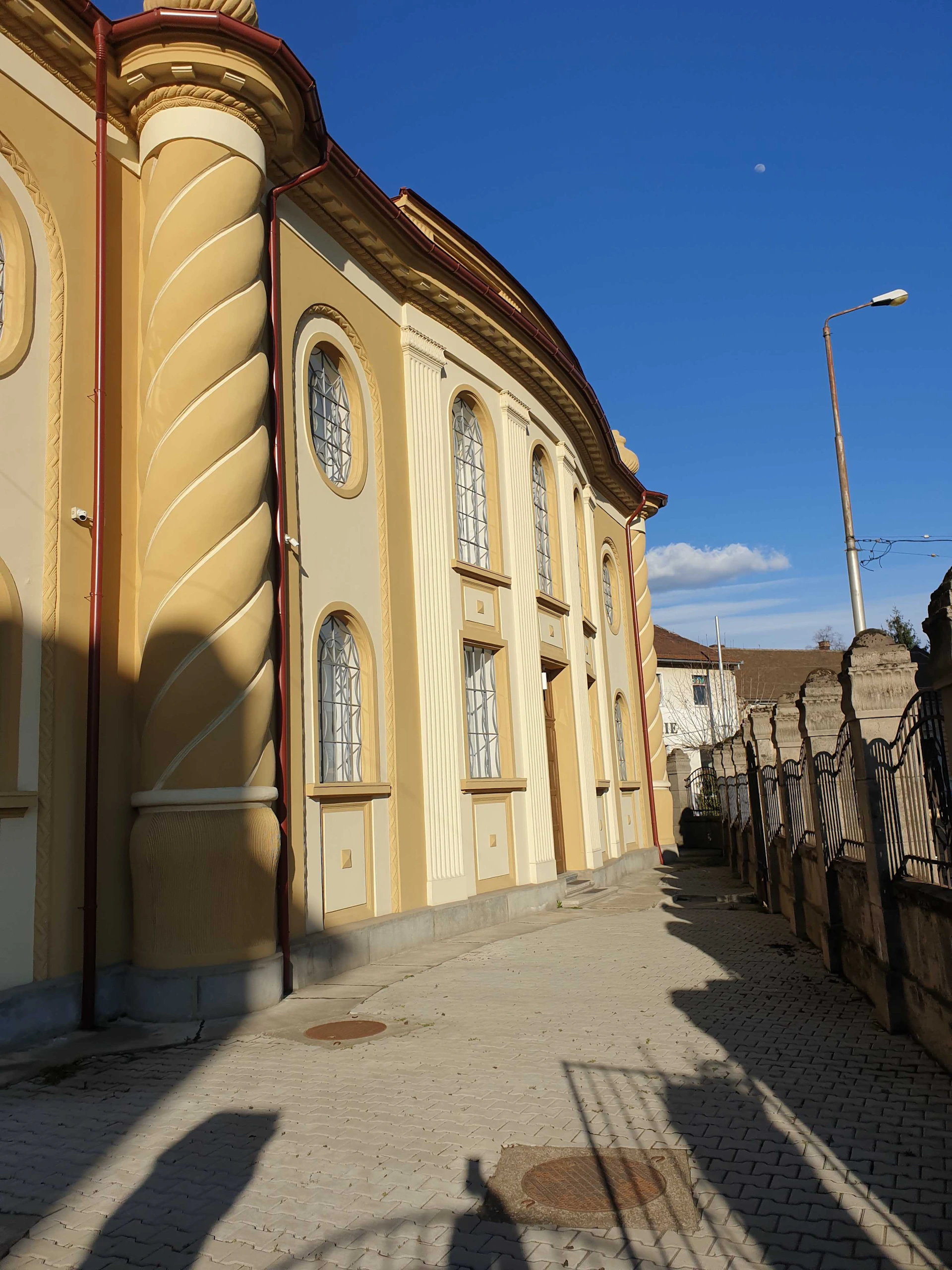 A yellow building with arched windows and twisted columns, next to a stone fence on a sunny day.