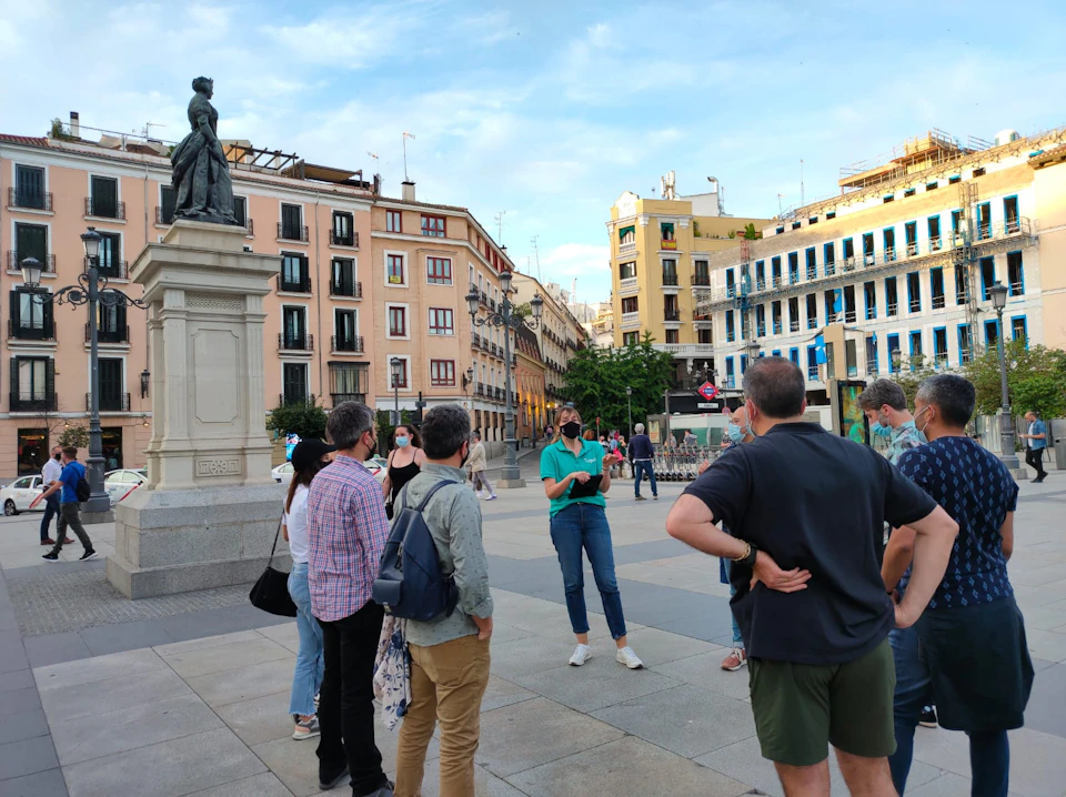 A group of people standing near a statue in a city square with historic buildings in the background.