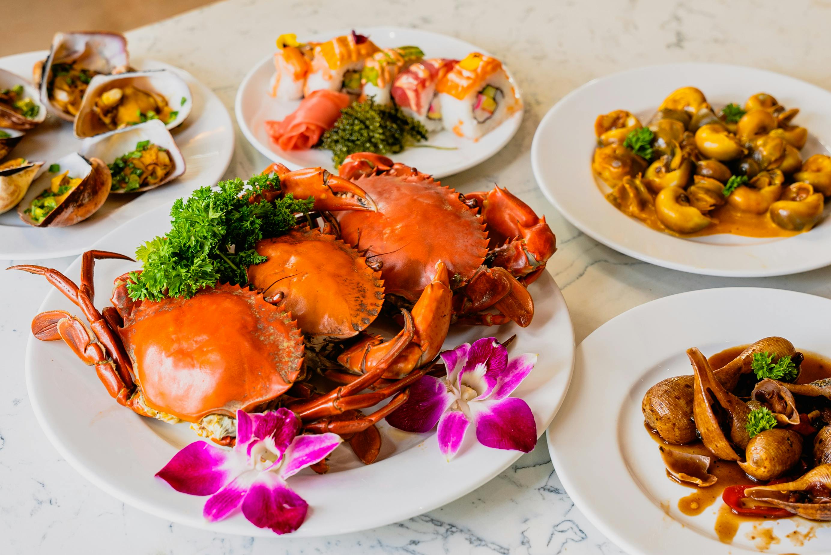 A table with a variety of dishes, including crabs garnished with herbs and flowers, sushi rolls, and a curry dish.