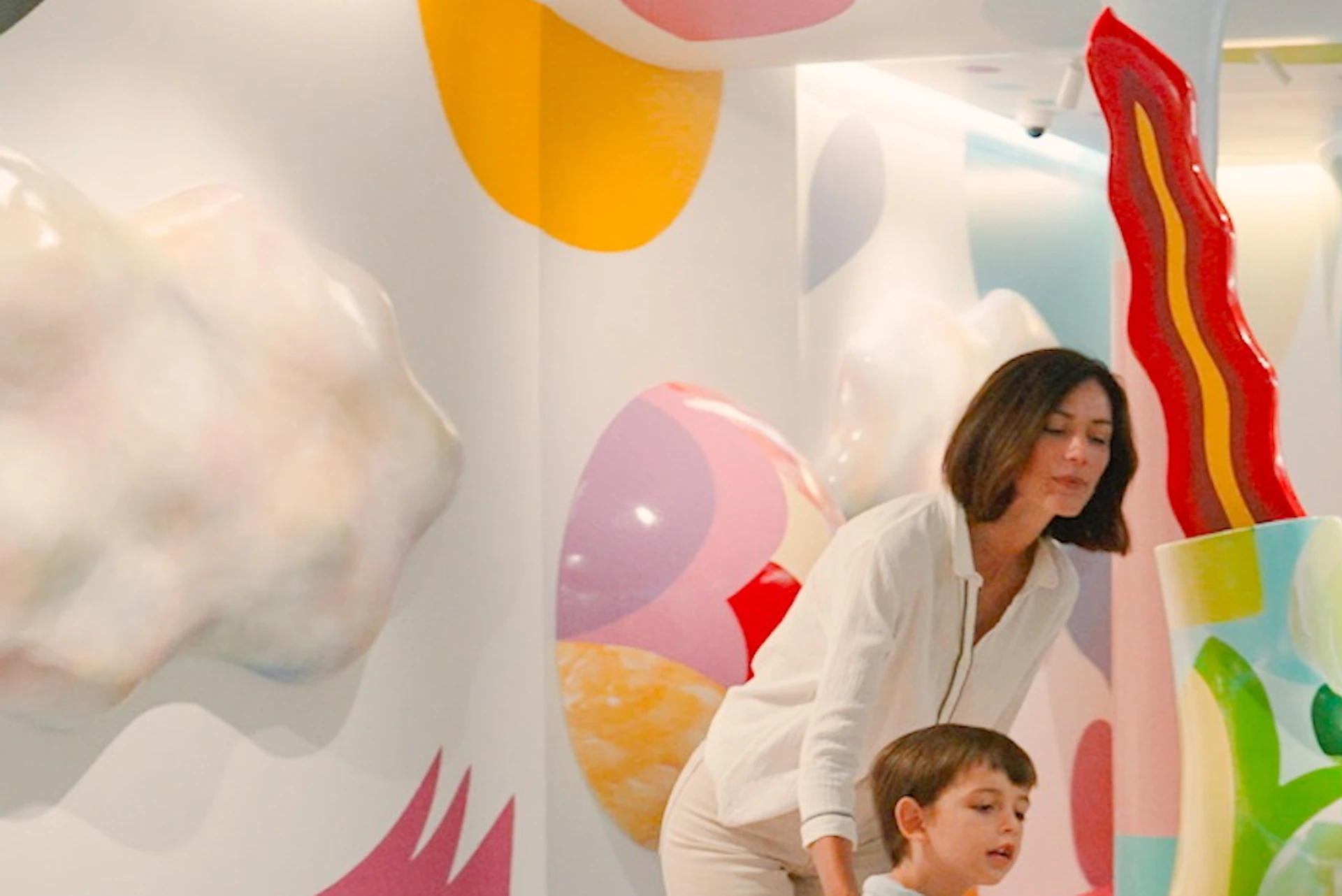 Three people interact with colourful, abstract sculptures in a vibrant, playful room covered with multicoloured murals.