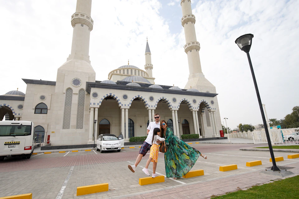 A family poses in front of a mosque with tall minarets on a partly cloudy day.
