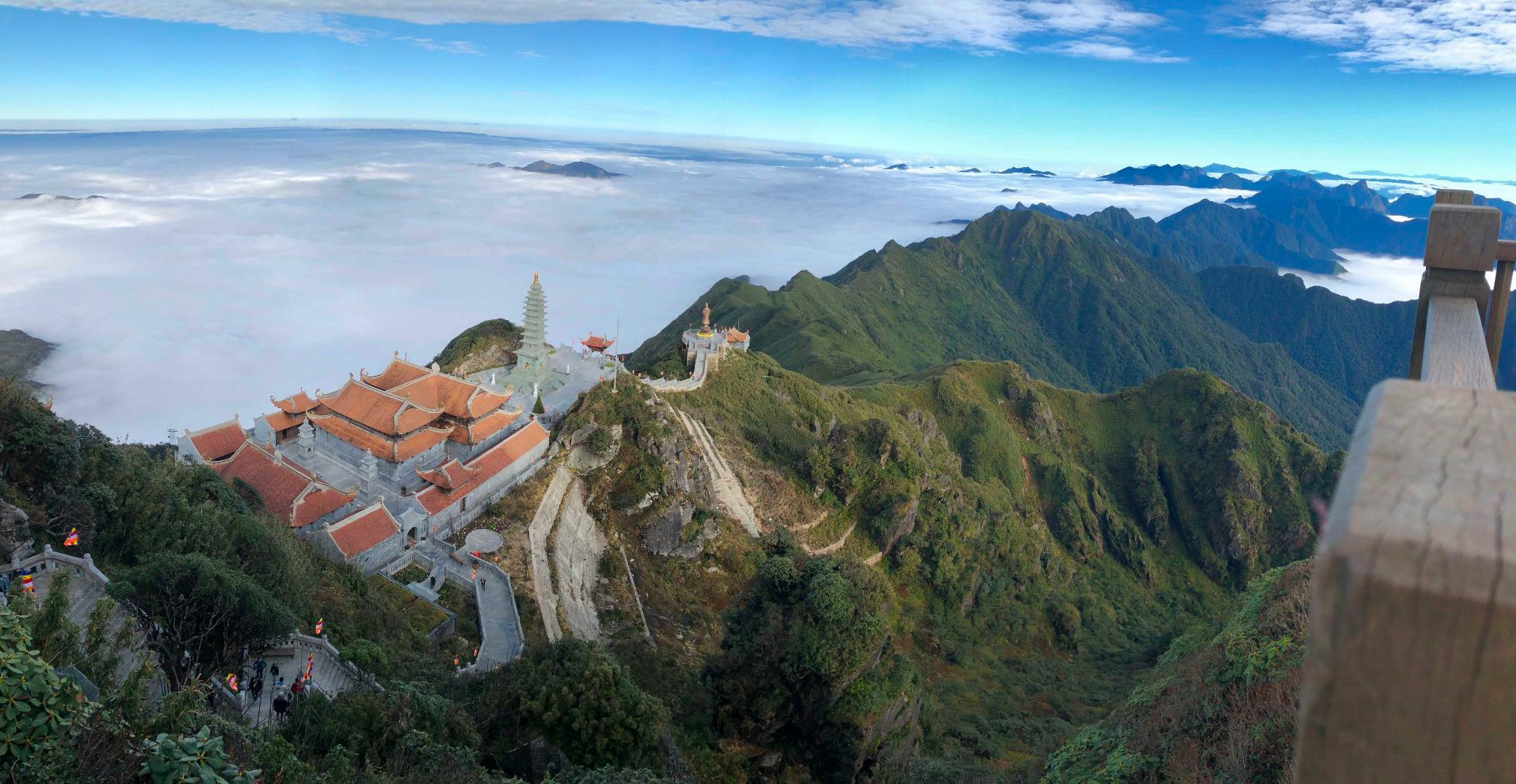 A mountain temple complex with traditional architecture, a pagoda, and paths, surrounded by lush greenery and a cloudscape.