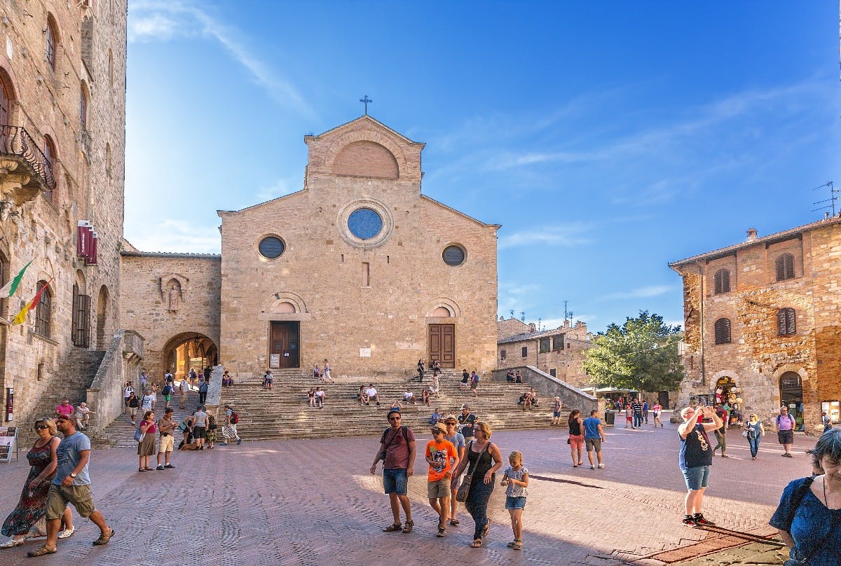 Ludzie idący i siedzący przed zabytkowym kościołem z dużą klatką schodową pod jasnoniebieskim niebem.
