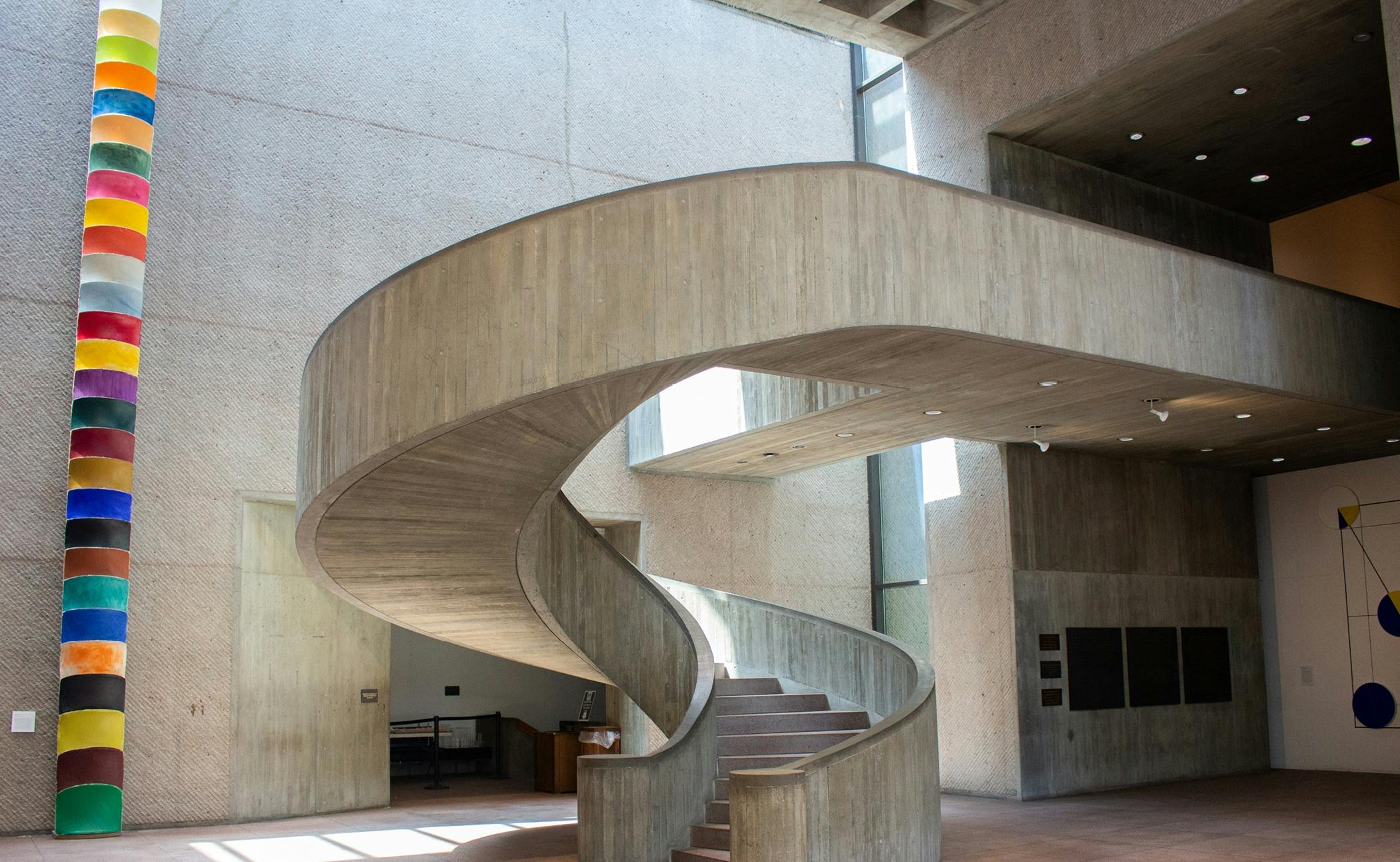 A modern interior space featuring a large, curved concrete staircase with natural light streaming from multiple windows.