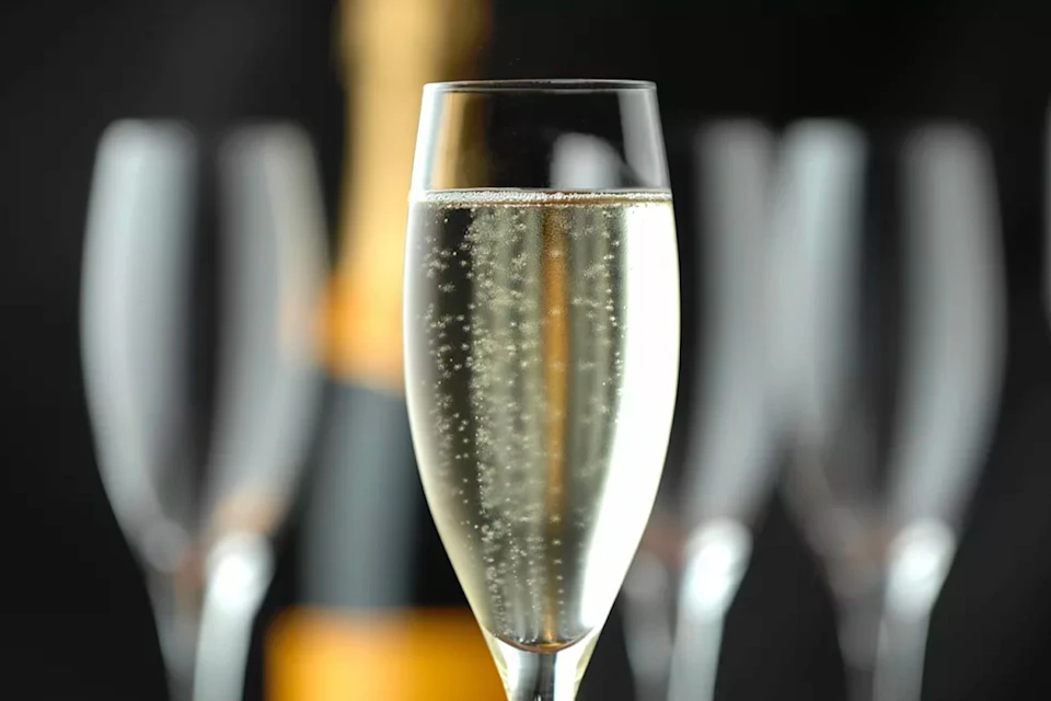 A close-up of a champagne flute filled with sparkling wine, with blurred champagne bottles and glasses in the background.
