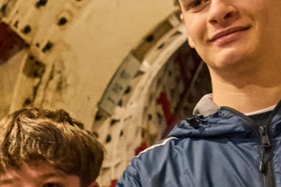 Two boys pose for a photo in a tunnel with a person taking their picture using a smartphone.