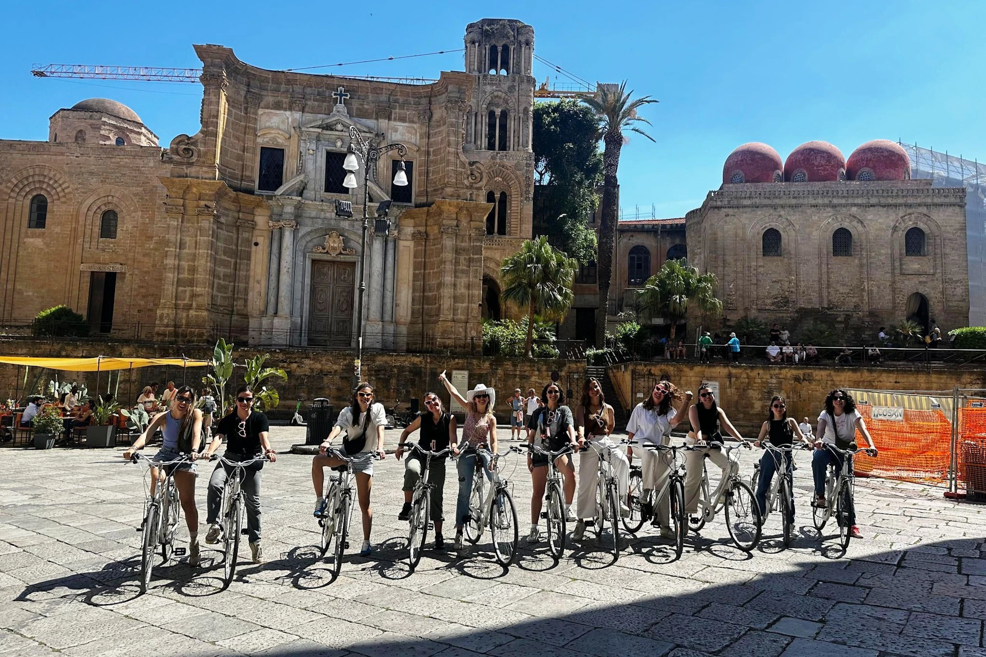 A group of people on bicycles posing in front of an ornate, historic building under a clear blue sky.