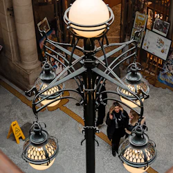 Utsmyckade taklampor i ett offentligt inomhusutrymme med människor som går, en "Varning våt golv" -skylt och omgivande affischer.