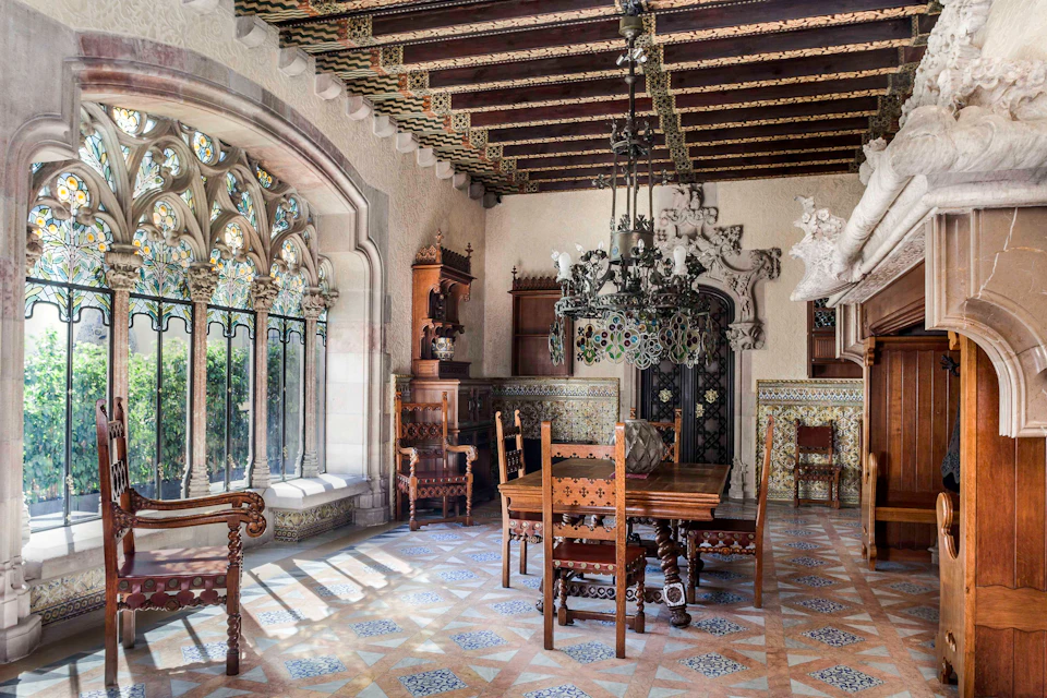 Ornately decorated dining room with wooden furniture, stained glass windows, a chandelier, and intricate ceiling and wall designs.