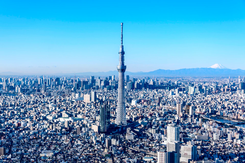 A tall tower in a cityscape under a clear blue sky, with mountains visible in the background.