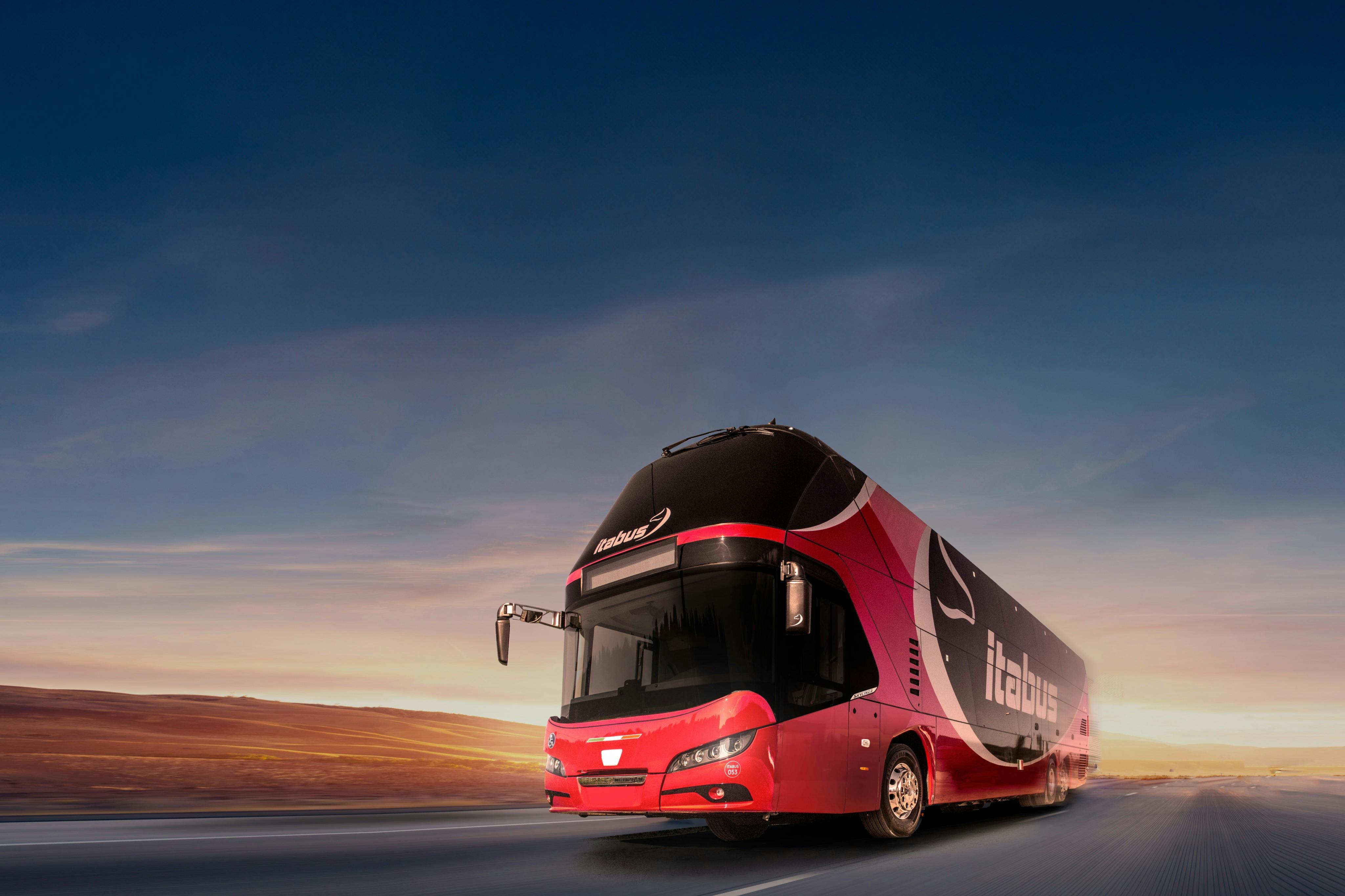 A red double-decker bus with "Itabus" branding drives on an empty road at sunset, against a clear sky.