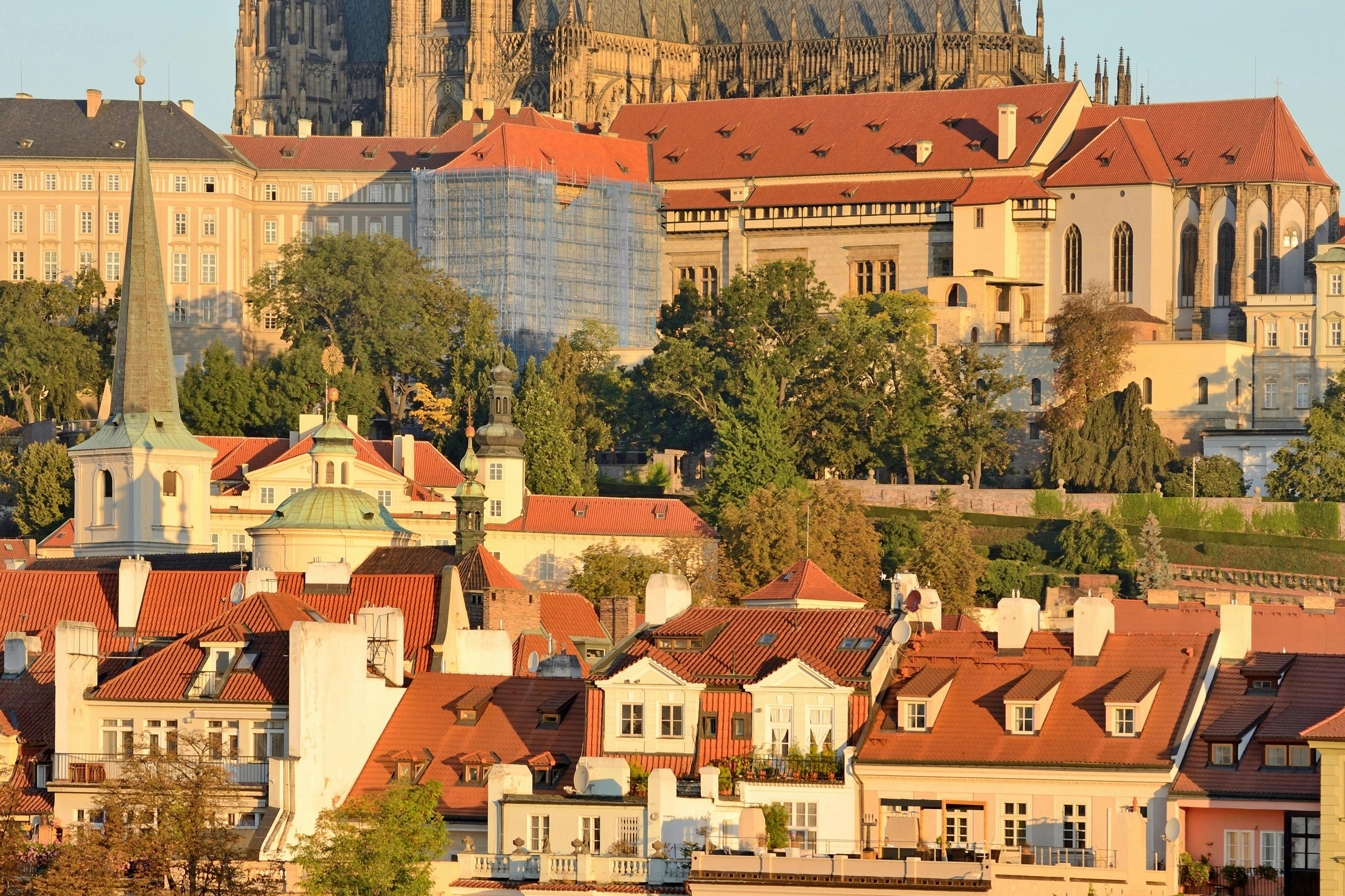 A scenic view of a historic city with red-roofed buildings, green trees, and a large cathedral in the background.