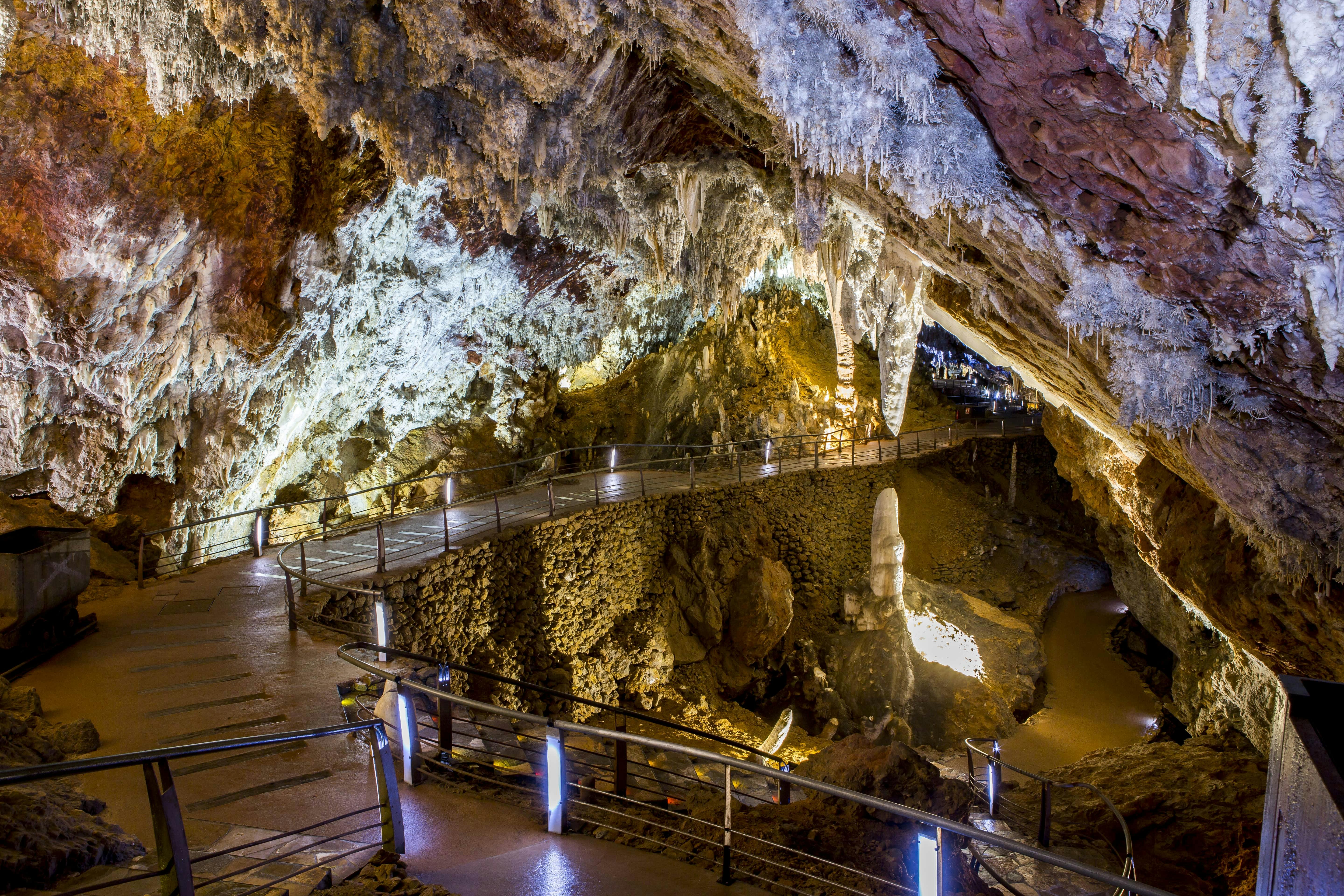 En veloplyst hule med en sti og rækværk, der viser stalaktitter, stalagmitter og klippeformationer.