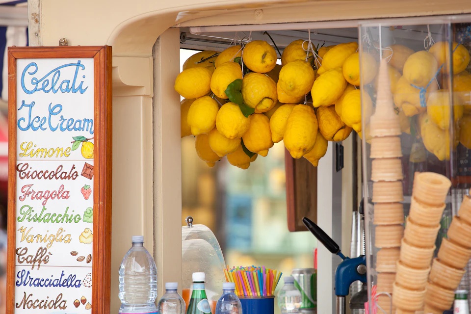 A close-up of a lemon stand with hanging lemons, water bottles, colorful straws, and an ice cream cone dispenser.