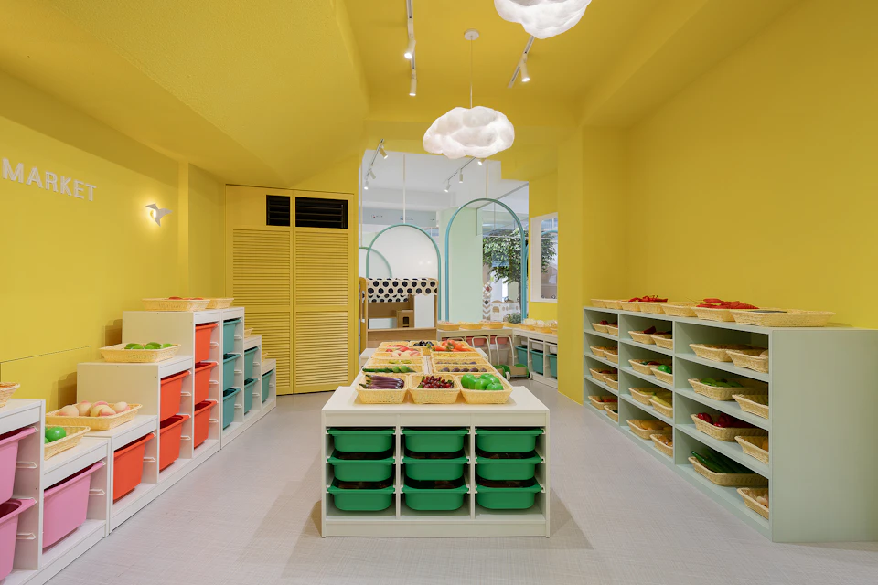 A brightly lit room with yellow walls, colorful storage bins, and tables displaying various fruits and vegetables.