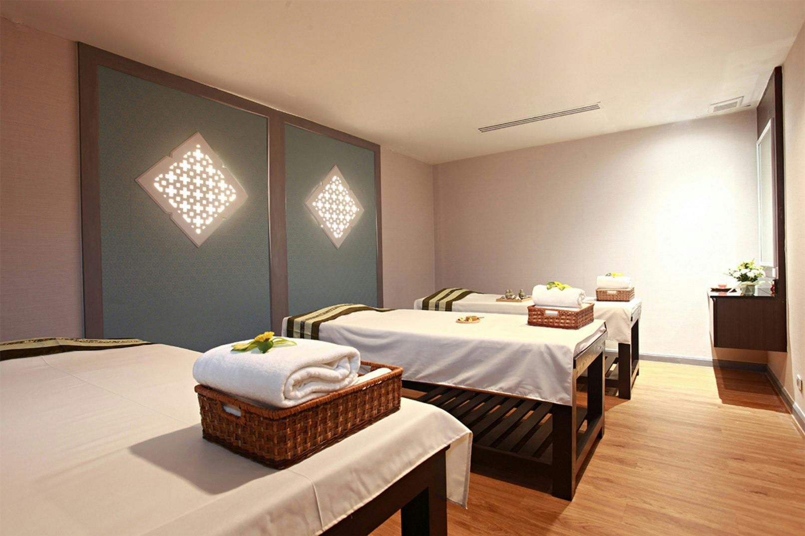 A spa room with four massage tables, each adorned with towels and decor, under soft lighting and decorative wall panels.