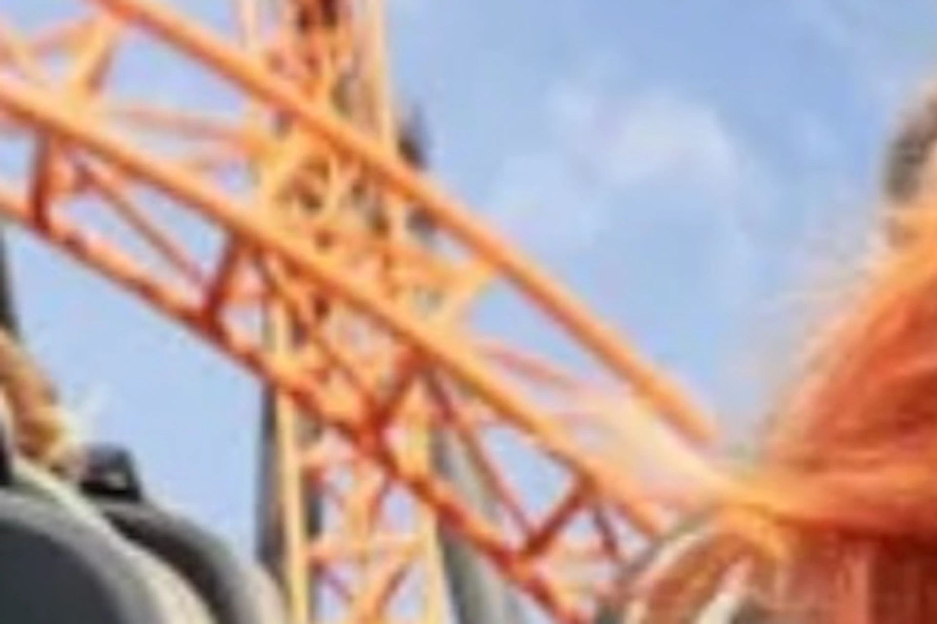 Two people riding a roller coaster with orange tracks under a blue sky; one is visibly excited.