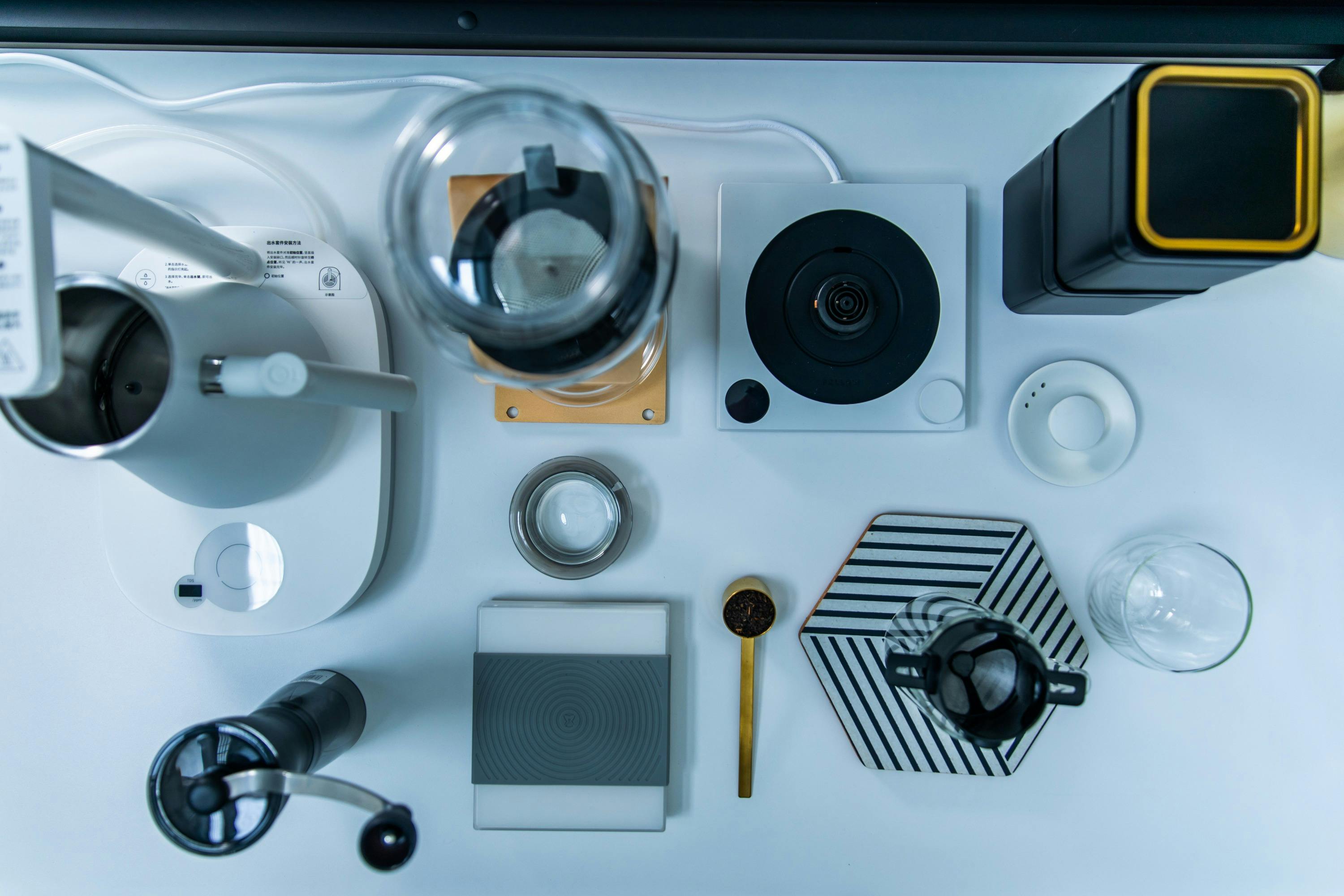 A top-down view of coffee-making equipment, including a grinder, scale, and brewing tools arranged neatly on a white surface.