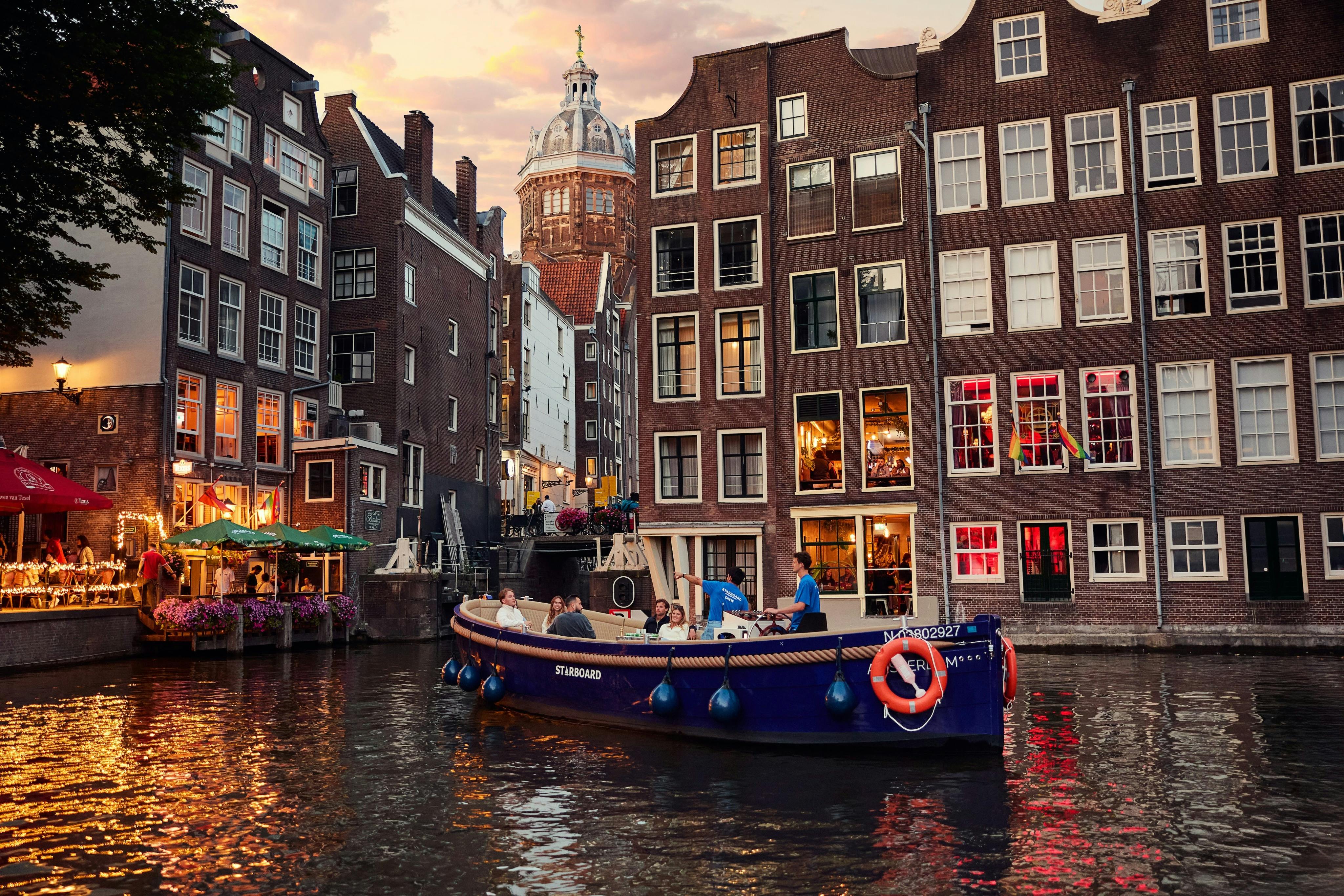 En kanalbåt med passagerare passerar historiska byggnader i en stadsbild i solnedgången.