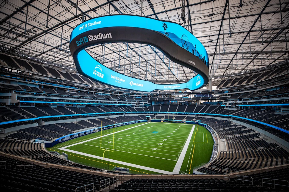 Empty stadium with a large, curved digital screen overhead displaying "SoFi Stadium" and a green football field below.