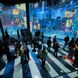 People standing and walking on a striped floor in a digital art installation with a futuristic cityscape backdrop.