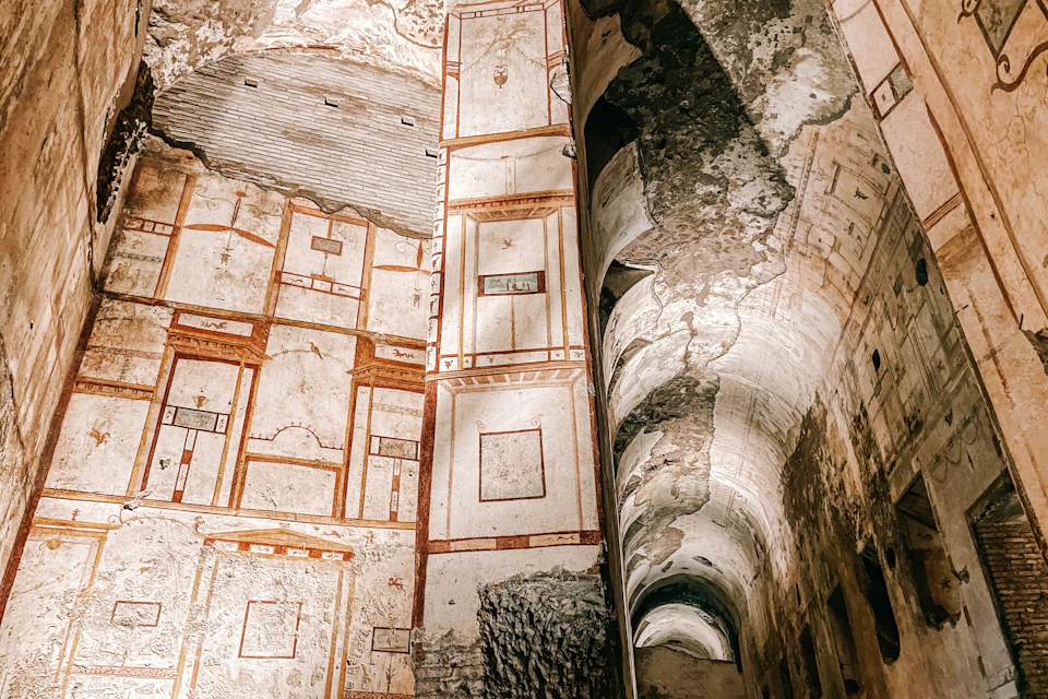 Interior of an ancient structure with faded murals and arches, showing aged walls and ornate designs.