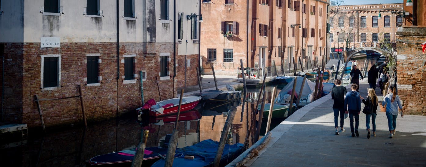 狭い運河に係留されたボートで歩いている人々は、晴れた日光の下でレンガ造りの建物に囲まれています。
