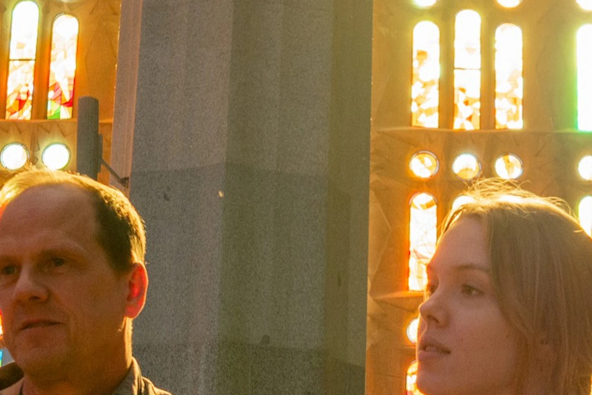 Three people stand inside a building with colorful stained glass windows, engaged in a conversation.