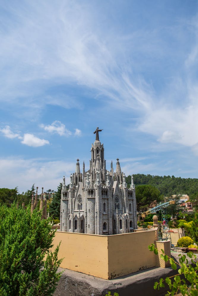 A detailed model of a Gothic-style cathedral with a statue on top, surrounded by trees and buildings under a partly cloudy sky.