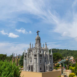 A detailed model of a Gothic-style cathedral with a statue on top, surrounded by trees and buildings under a partly cloudy sky.