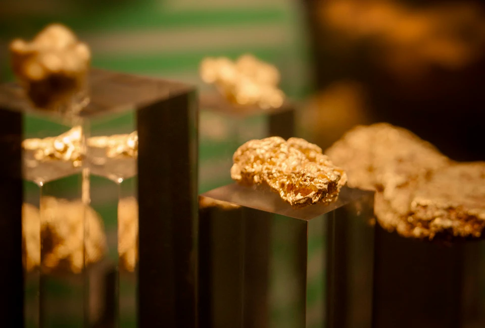 Golden nuggets displayed on glass pedestals with a blurred green and yellow background.