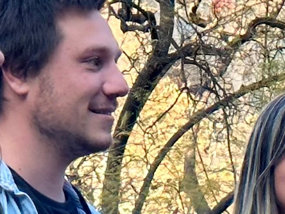 Four people stand together, smiling, in front of the Sagrada Familia. A crane and trees are visible in the background.