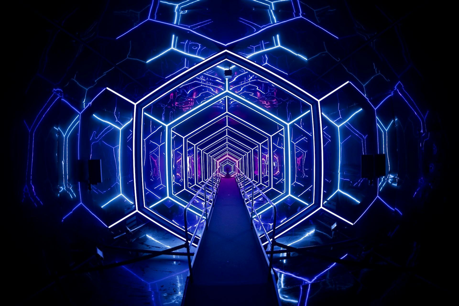 A futuristic, hexagonal tunnel illuminated with vibrant blue and purple neon lights, creating a deep, perspective effect.