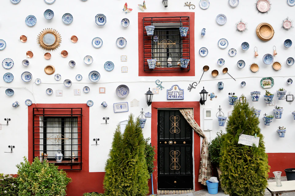 White wall with red-trimmed windows and doors, adorned with various decorative plates, pots, and plants.
