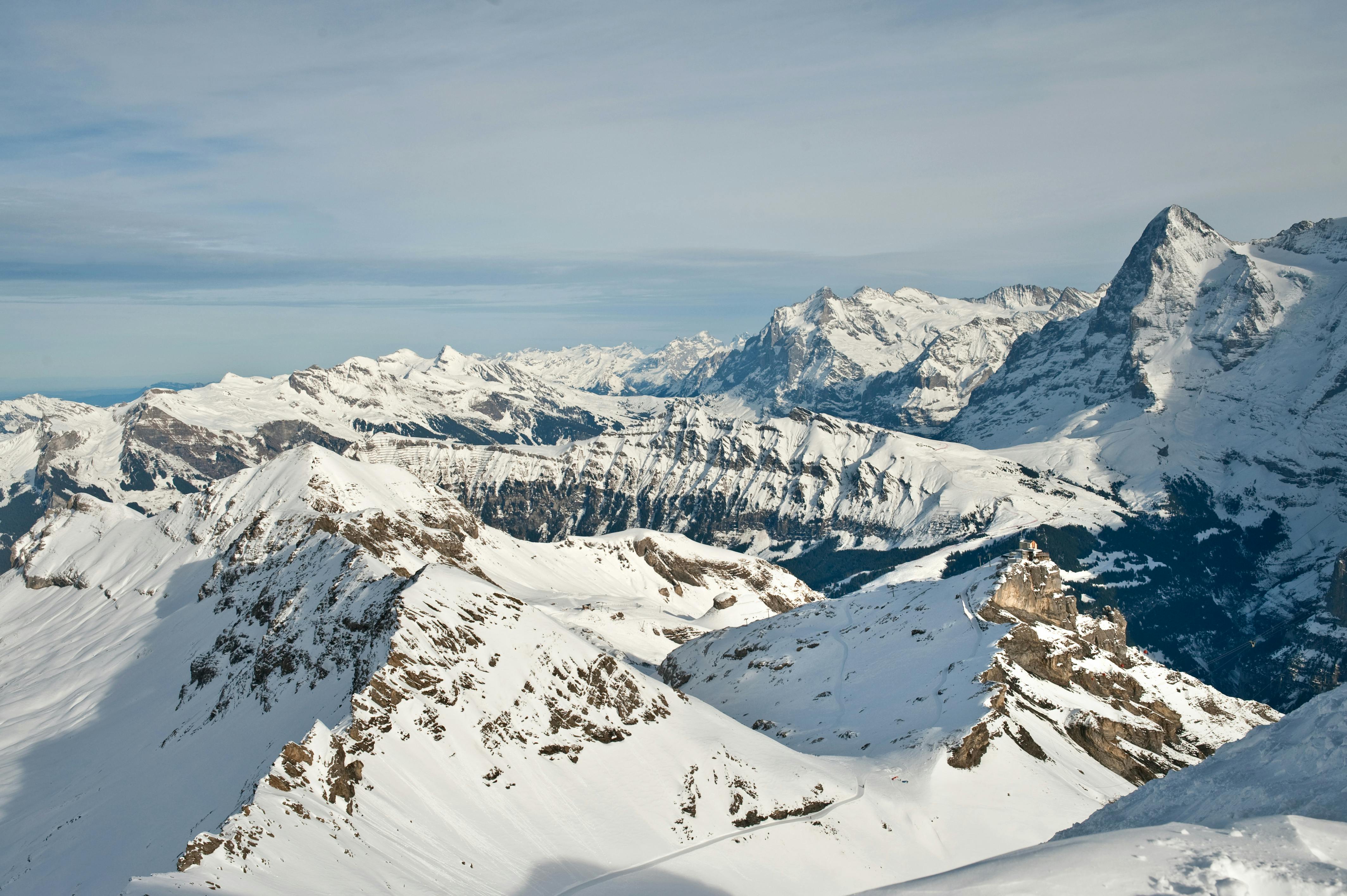 Χιονισμένη οροσειρά κάτω από έναν συννεφιασμένο ουρανό, με τραχιές κορυφές και κοιλάδες που εκτείνονται σε απόσταση.