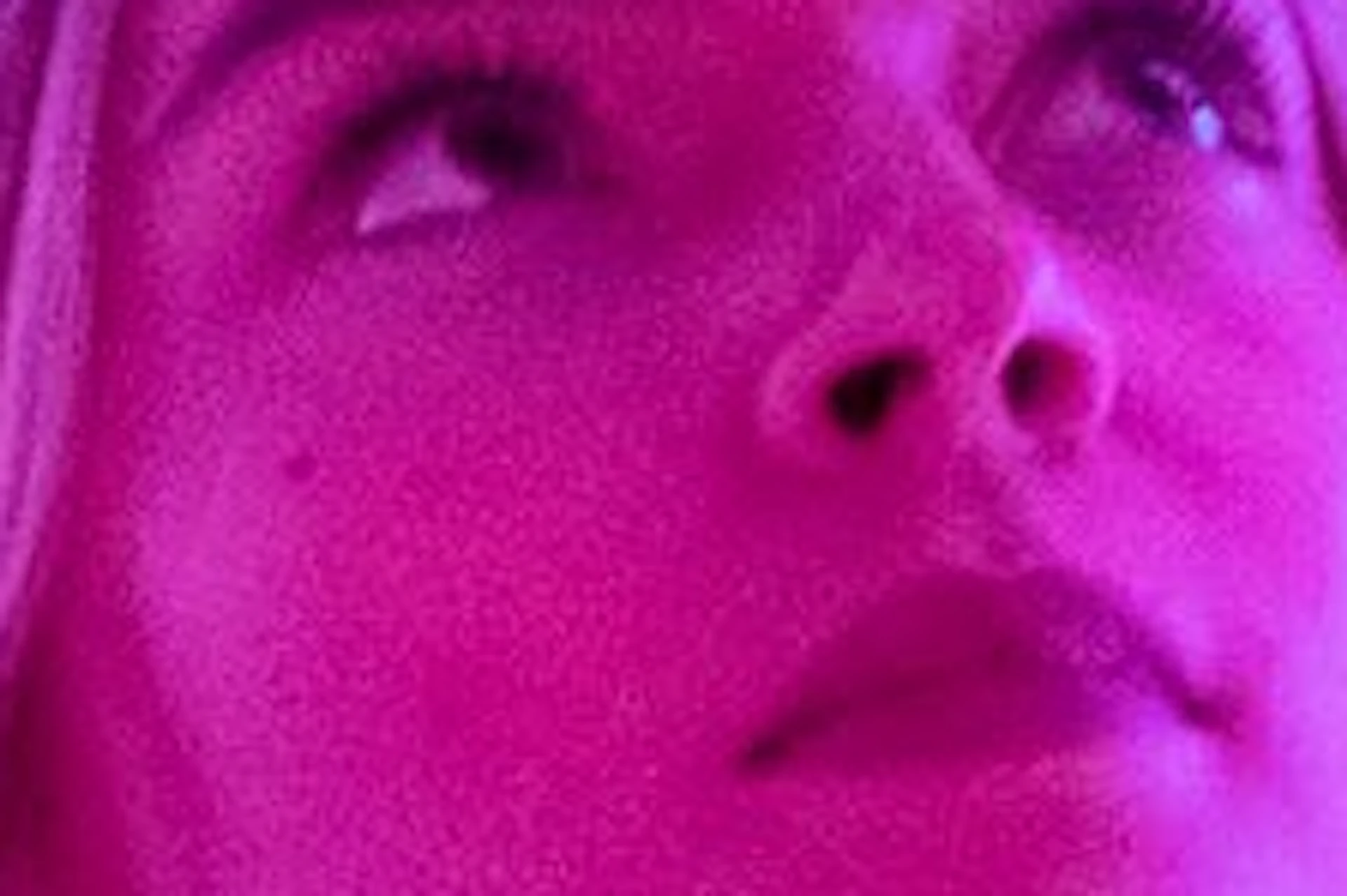 A person stands in a room with reflective walls and neon pink and purple lighting, creating a kaleidoscopic effect.