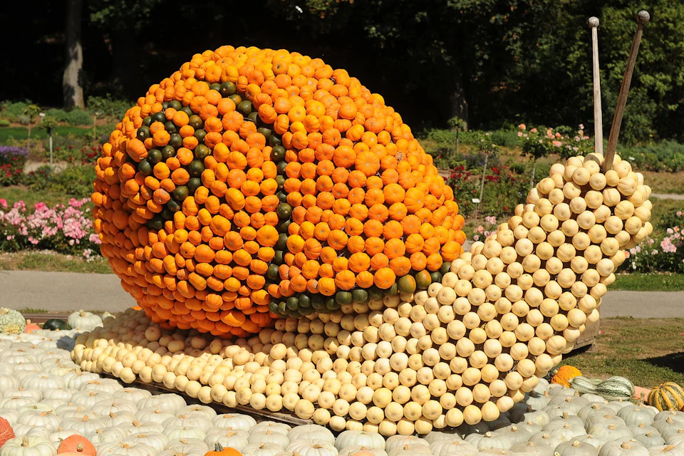 A large sculpture of a snail made entirely of orange and white pumpkins, displayed outdoors in a garden setting.