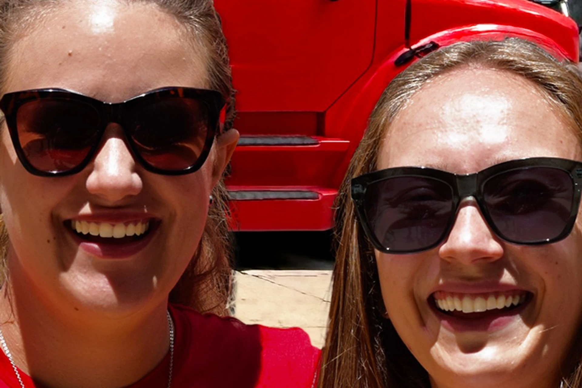 Two women in red shirts with Chicago Crime Tours branding pose in front of a red and yellow tour bus with crime-themed graphics.