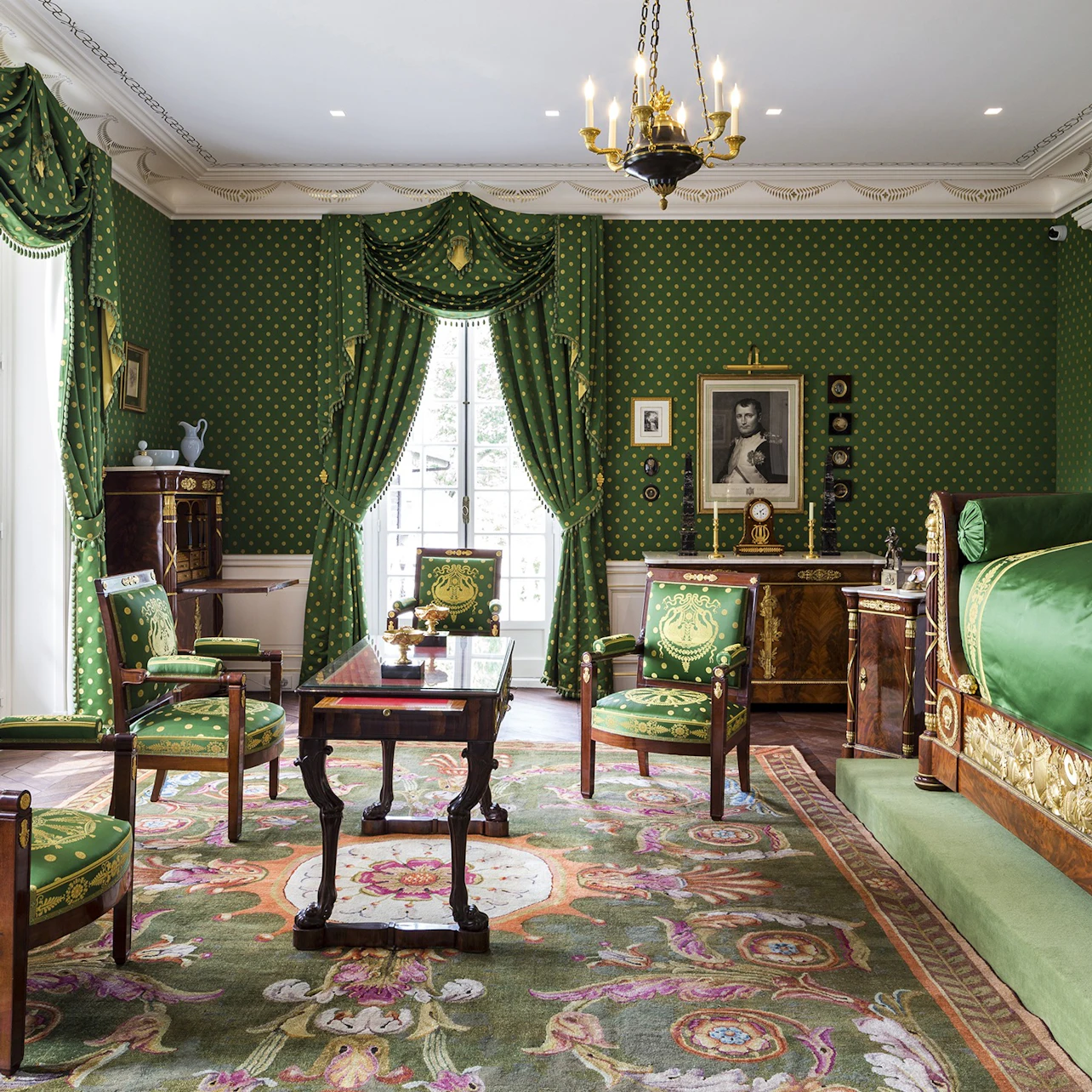 A luxurious room with green wallpaper and curtains, ornate furniture, a chandelier, and a decorative rug.