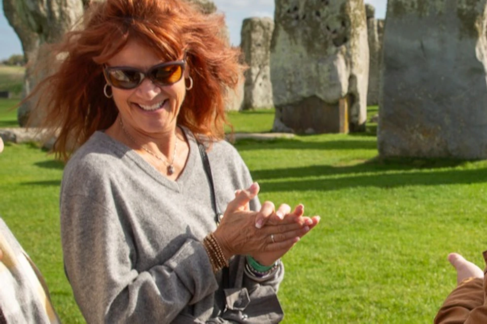 A group of people talking and smiling in front of the Stonehenge monument on a sunny day.