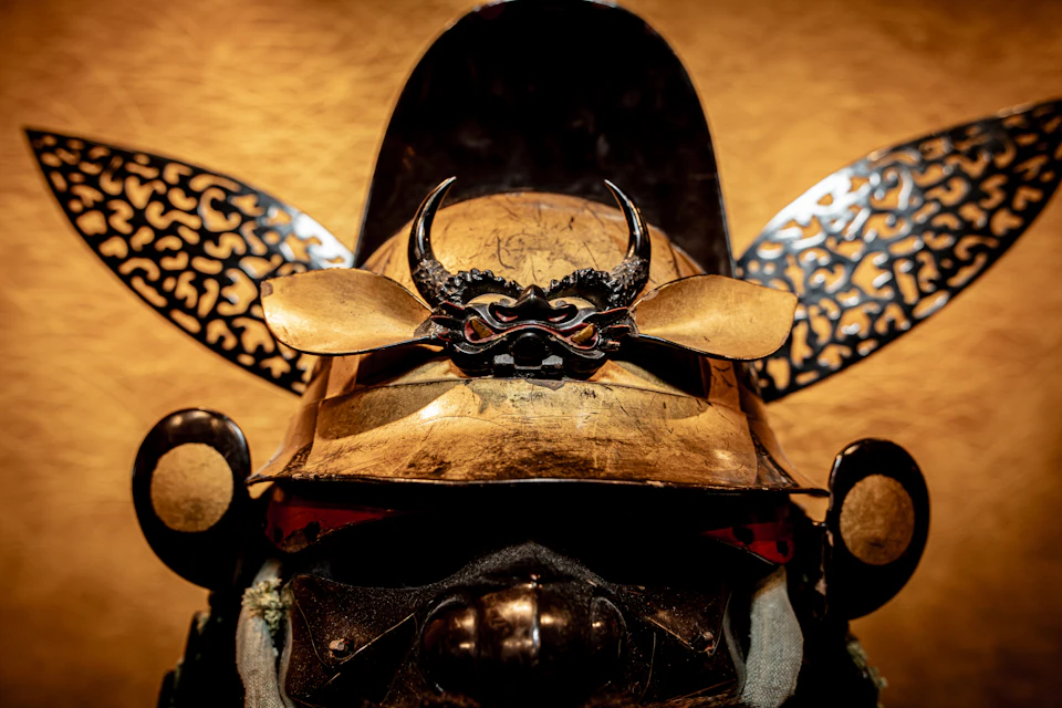 A traditional Japanese samurai helmet with ornate details and horn-like ornaments, displayed against a golden background.