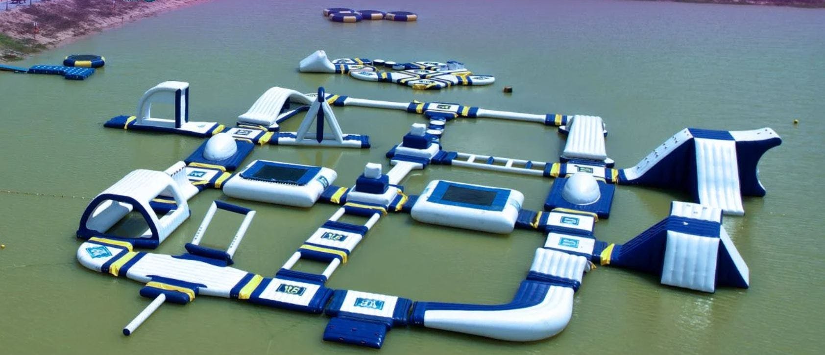 Inflatable water park with various interconnected structures and obstacles floating on a lake.