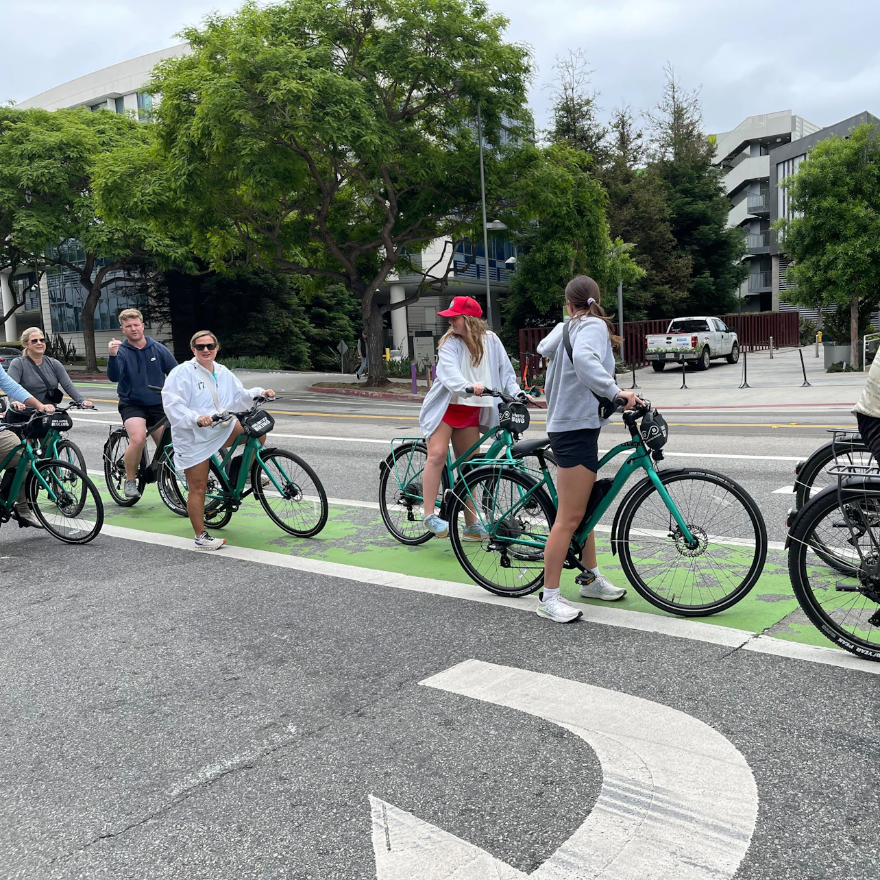 A group of people standing with bicycles in a designated bike lane on a city street lined with trees and buildings.