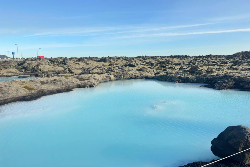 Bright blue lagoon surrounded by black volcanic rocks under a clear blue sky.