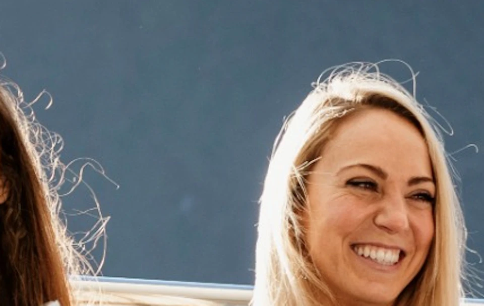 Four people sitting on a boat deck, smiling and holding drinks, with mountains in the background on a sunny day.