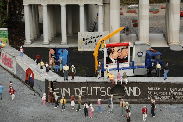 Maqueta d'una escena històrica que representa el mur de Berlín amb persones en miniatura, grafitis, equips de construcció i edificis adjacents.
