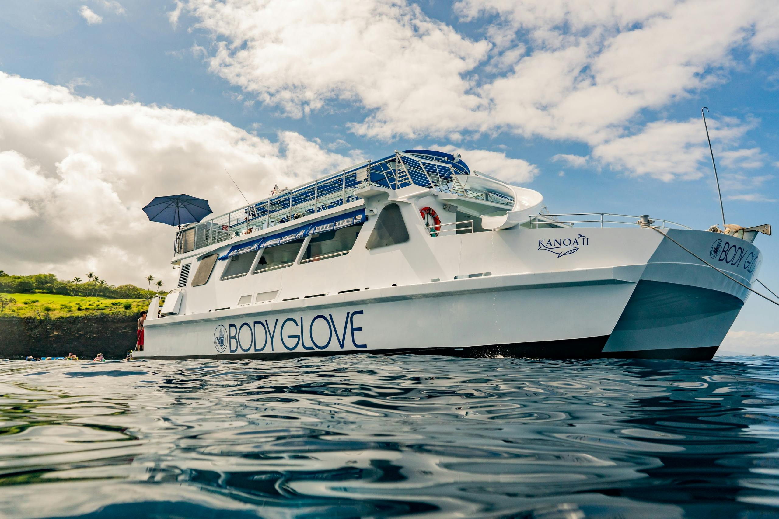 A white boat named Kanoa II with "Body Glove" branding is on the water under a partly cloudy sky.
