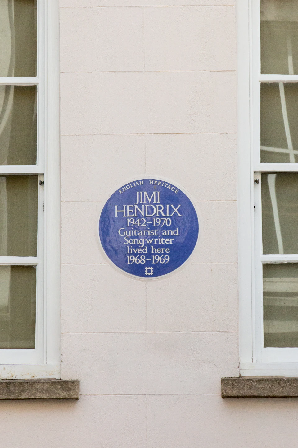 Blue plaque on a beige wall between two windows reads: "Jimi Hendrix 1942-1970 Guitarist and Songwriter lived here 1968-1969."